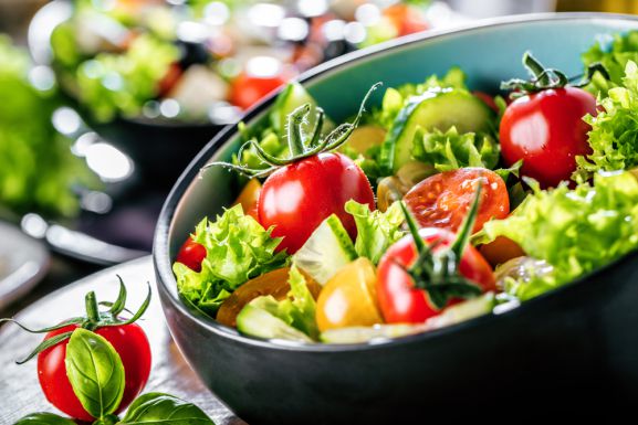 Schwarze runde Schüssel mit grünem Salat, Tomaten und Paprika